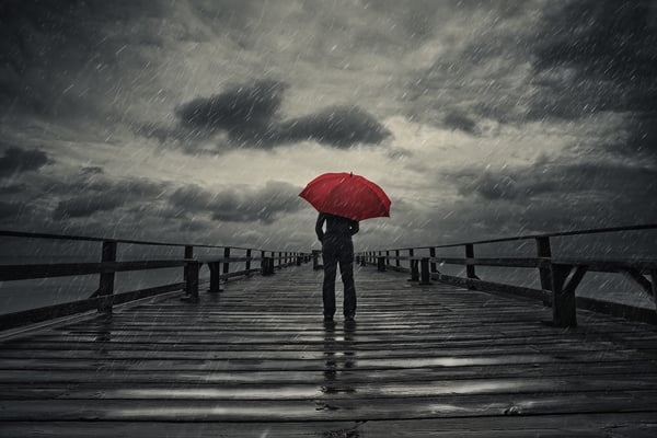 Person standing on a pier during a storm with a red umbrella